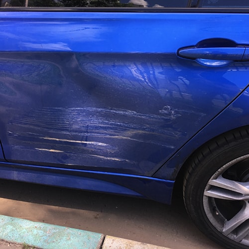 Поврежденная дверь автомобиля после ДТП (деформация и повреждение лакокрасочного покрытия)